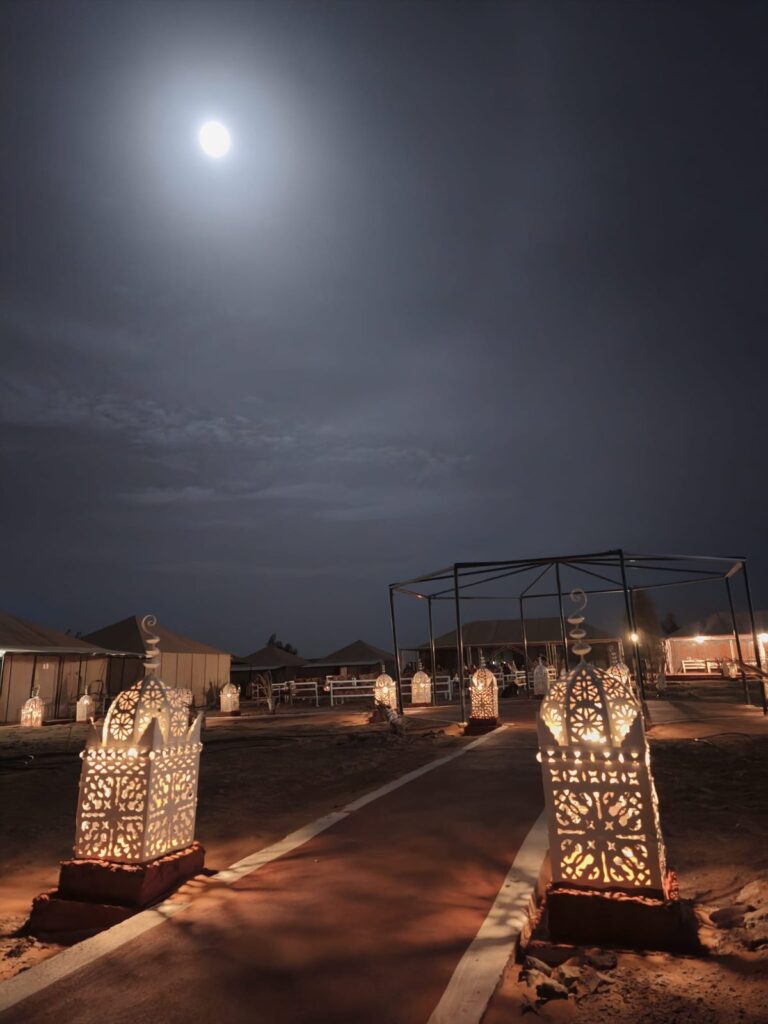 Lantern-lined path through a desert camp under a full moon