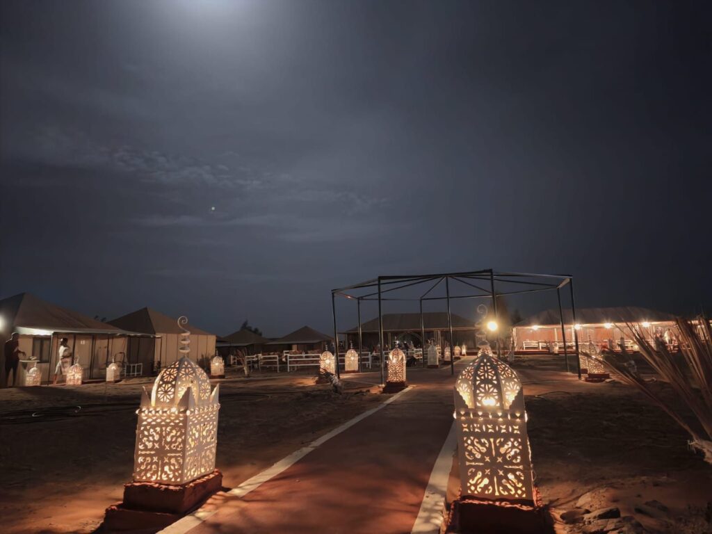 Carved lanterns lighting the path through a desert camp under the moon