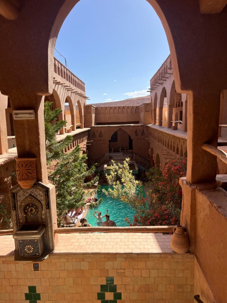 A pool in an earthen kasbah courtyard seen through an arch