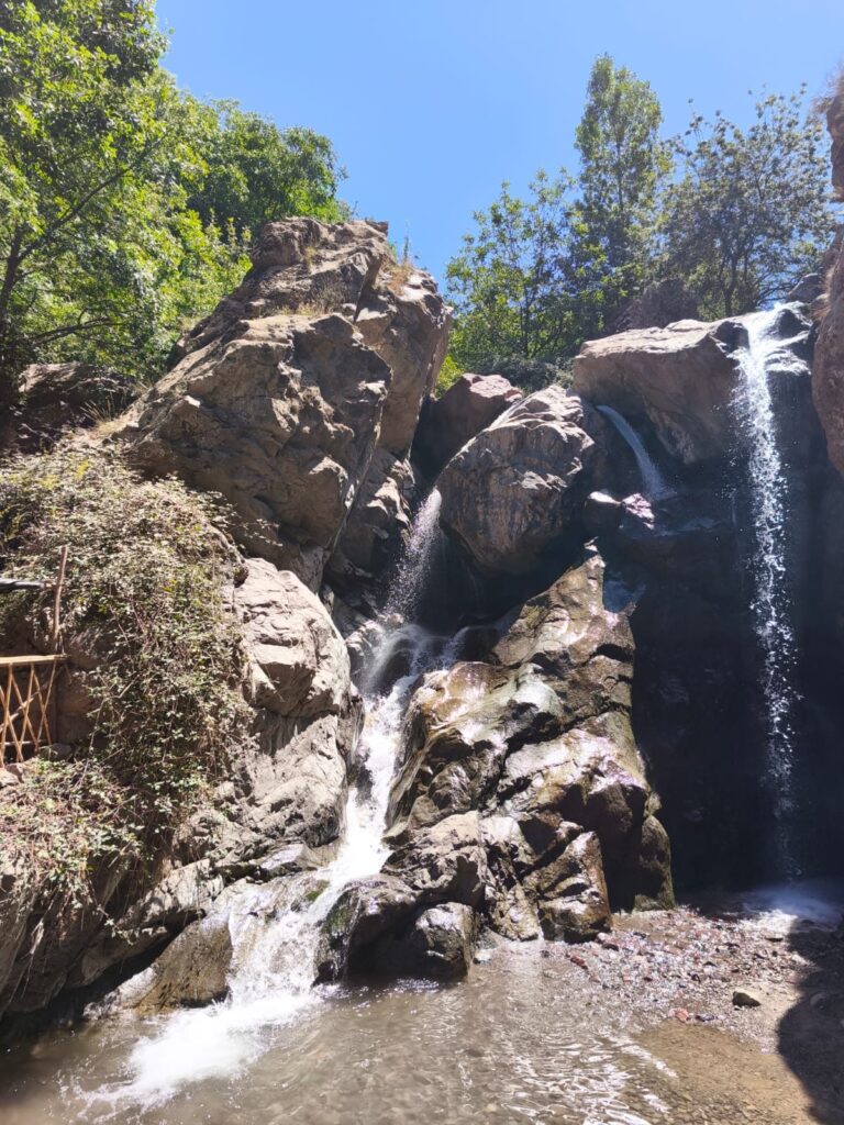 A waterfall pouring over boulders under green trees
