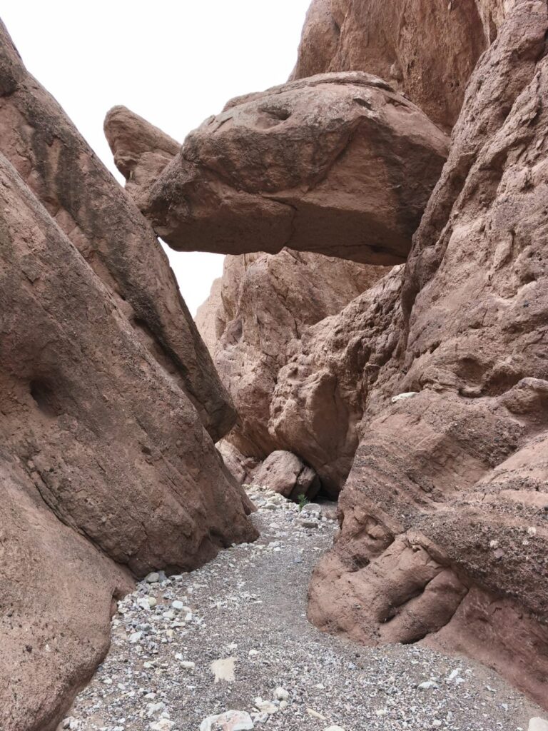 A boulder wedged between the walls of a narrow red-rock canyon