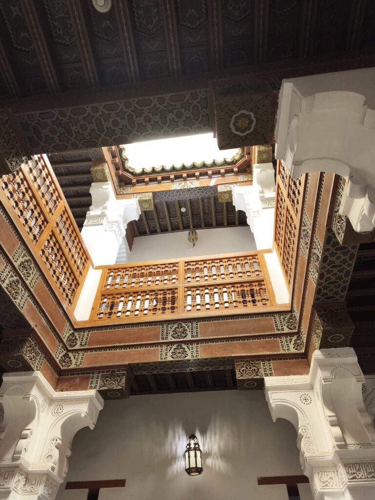 Carved cedar balconies and a painted ceiling around a riad courtyard